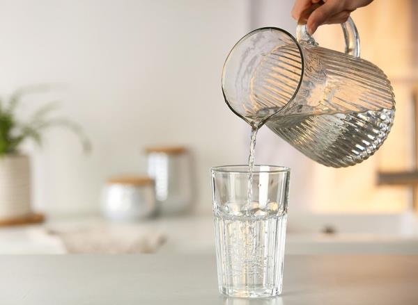 A glass pitcher pouring a glass of water