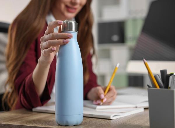 A woman at her desk using a blue water bottle with a me<em></em>tal cap