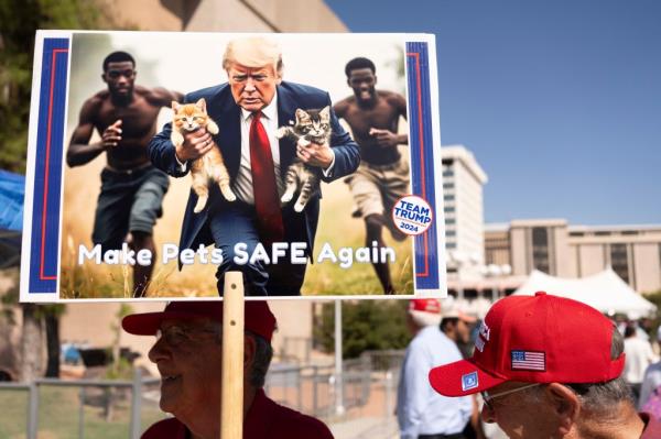 A man carries an AI-generated image of former US President and Republican presidential candidate Do<em></em>nald Trump carrying cats away from Haitian immigrants.