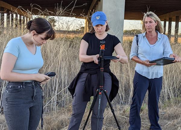 In a field, three adults set up audio and video equipment to mo<em></em>nitor wildlife. 