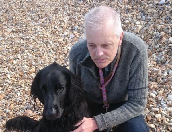 A man with a black dog on a pebbly beach.