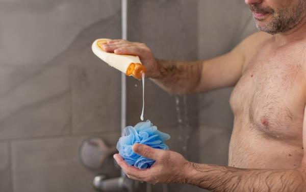 man putting soap on a loofah in the shower