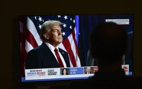 Do<em></em>nald Trump on a television screen being watched by a silhouetted man