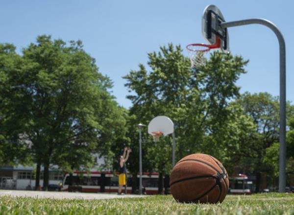 A basketball on the grass in front of a basketball hoop on a court.