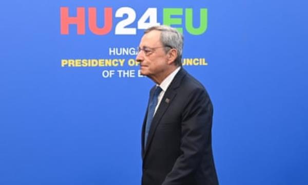 Mario Draghi arrives at the Puskas Arena in Budapest, 8 November 2024: he is striding purposefully past a sky-blue backdrop with the summit’s logo and lettering that reads HU24EU 