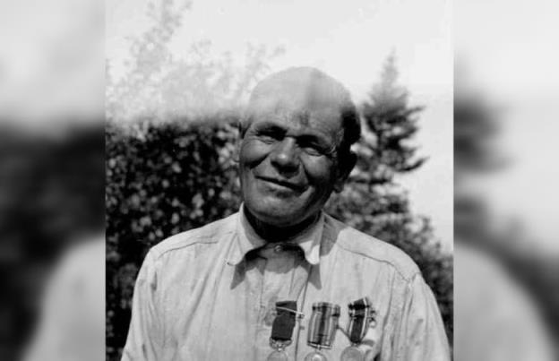 A black and white photo of an older, bald man, wearing three medals. 