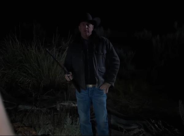 Kevin Costner holding a gun in the dark. 