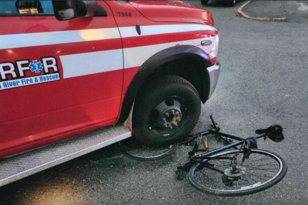 The front wheel of a bicycle is crushed under the front right wheel of an ambulance.