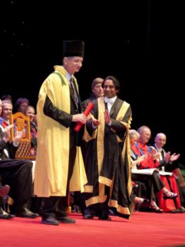 Geoffrey Hinton receives an ho<em></em>norary degree on stage, standing next to Chancellor Sanjeev Bhaskar OBE