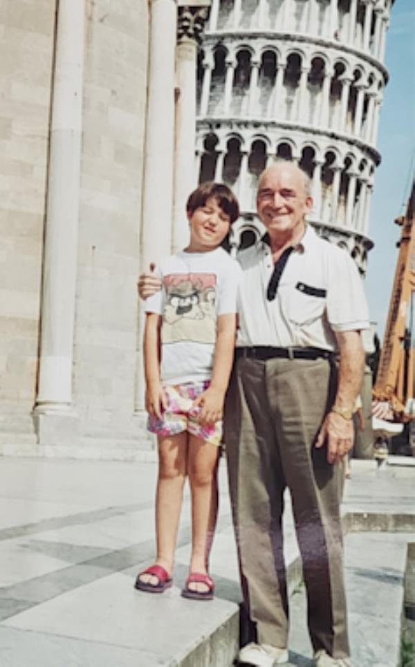 A boy and his grandfather on holiday in front of the leaning tower of Pisa.