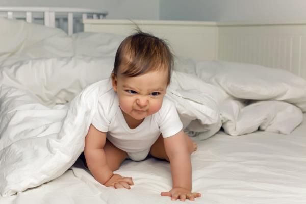 A baby crawling out from under a white duvet.