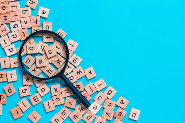 A magnifying glass over a scattering of wooden scrabble tiles on a blue background