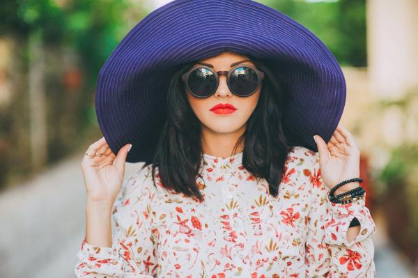 A fashio<em></em>nable woman wears sunglasses and a big hat.