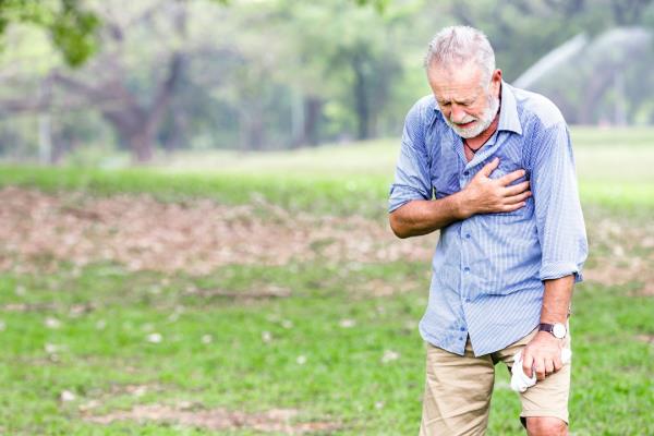 A elderly man outdoors, clutching his chest.