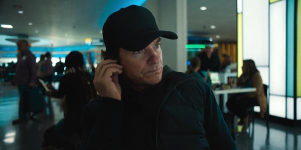 Jason Bateman in all black looking intense and checking his earpiece in Carry-On